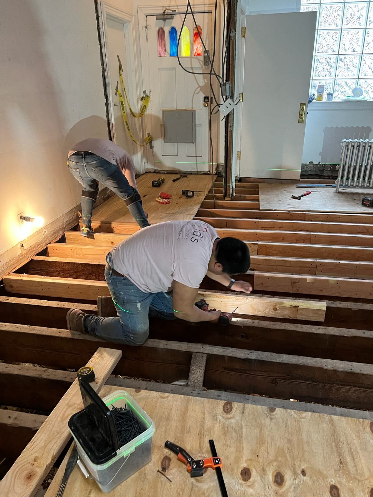 Construction crew performing beam-to-beam floor leveling and installing new subfloors.